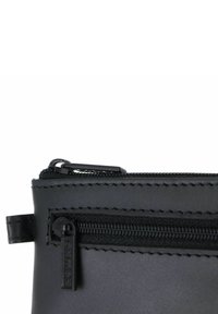 Pochette en cuir noir avec fermeture éclair, présentant des détails de couture et une petite tirette de zipper marquée. Texture lisse avec une finition mate.