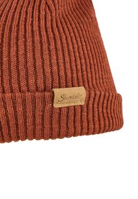 Rust-colored knitted beanie with ribbed texture, featuring a folded brim and a brown leather tag with embossed text.