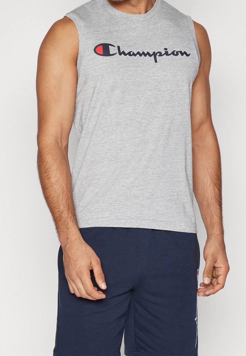 Homme portant un débardeur gris Champion et un short bleu marine, debout avec les bras détendus le long du corps.