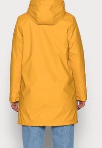 Żółta wodoodporna parka z kapturem, o gładkiej, błyszczącej fakturze i długich rękawach, sięgająca do połowy uda z bocznymi kieszeniami.