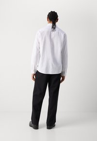 Camisa blanca de manga larga con un acabado texturizado, dobladillo curvado y puños abotonados, combinada con pantalones negros de pierna ancha y zapatos negros.