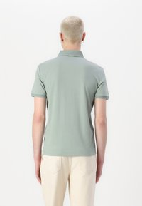 Zeleno bombažno polo majico s klasičnim ovratnikom in kratkimi rokavi, ki se ponaša z diskretno teksturo in kontrastnim robom ob ovratniku.