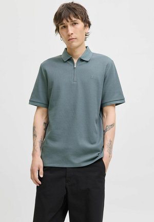 Polo shirt i teal, lavet af textured stof, med en lynlåskrave og korte ærmer, parret med sorte bukser.