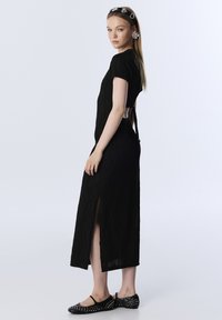 Zwarte midi-jurk met een gestructureerd golfpatroon, korte mouwen, een zijsplit en een uitgesneden rug. Gekocht met zwarte studschoenen.