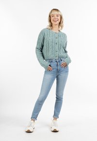 Ljus teal kabelstickad cardigan med rund hals, sex knappar och ribbat avslut. Kombinerad med ljusblå slim fit jeans och vita sneakers.