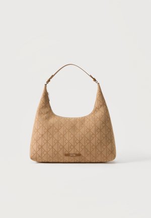 Beige Calvin Klein skuldertaske med monogrammønster, buet toplynlås og enkelt justerbart rem mod ensfarvet baggrund.