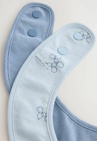 Deux bavoirs pour bébé bleus superposés avec des boutons-pression, l'un uni bleu clair et l'autre bleu clair avec des motifs de ballons dessinés en lignes simples.