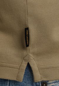 Khaki katoenen trui met een split aan de onderkant, gedetailleerde stiksels en een zwart label met "PME LEGEND" in goud. Draagt over blauwe denim.