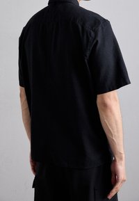 Zwart T-shirt met korte mouwen, gemaakt van lichte stof, met een kraag en een relaxte pasvorm, met een gladde textuur en een minimalistisch ontwerp.