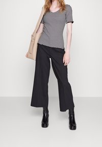 Black and white striped short-sleeve top with ruffled hem paired with wide-leg black trousers and black heeled ankle boots. Beige bag on shoulder.