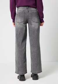 Hochtaillierte, weit geschnittene graue Denim-Jeans mit einem ausgewaschenen Finish, ausgestattet mit zwei hinteren Taschen und rohen Säumen. Getragen mit schwarzen Plateaustiefeln.