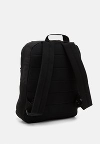 Sac à dos en tissu noir avec panneau arrière rembourré, bretelles ajustables et poignée supérieure. Présente un design minimaliste et un matériau solide.