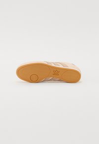 Világos barack színű gumis sneaker talp, texturált rágó aljjal. Három vízszintes csíkkal és bélyegzett logóval a saroknál. Simább anyagfelület.