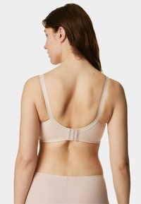 Sujeción color beige claro con tela lisa, tirantes ajustables y cierre de gancho en la parte trasera. Presenta un diseño sin costuras y con detalles mínimos.