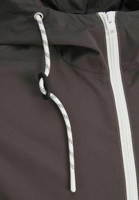 Brown zippered jacket with a white zipper and cord. Cord features black dots and a black toggle for adjustment. Smooth, water-resistant fabric.