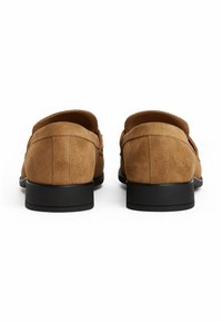Suede loafers in light brown with a smooth texture, low black rubber soles, and stitched detailing on the upper.