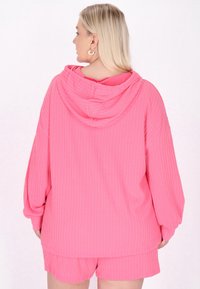 Felpa rosa con cappuccio, dalla texture a coste e vestibilità oversize, abbinata a pantaloni shorts coordinati, con maniche e orlo rilassati.