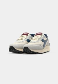 Sneakers with a cream mesh upper, gray suede accents, blue side stripes, and black rubber outsole; maroon branded tongue detail.