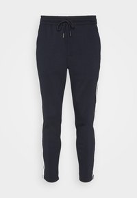 Pantalon de survêtement bleu marine en tissu doux avec une taille élastique et un cordon de serrage ajustable. Doté de rayures blanches sur les côtés et de jambes fuselées.