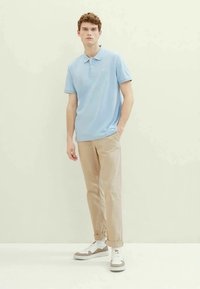 Polo bleu clair, à manches courtes, col. Chinos beiges, coupe slim. Baskets grises et blanches avec un accent marron. Design simple, texture lisse.
