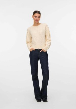 Maglione beige lavorato a maglia con un motivo testurizzato e scollatura rotonda, abbinato a jeans blu scuro e calzature nere. Vestibilità casual, maniche lunghe.
