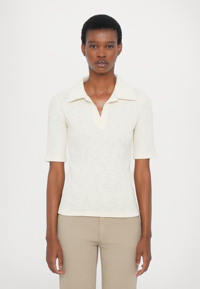 Cămașă polo tricotată în off-white, cu decolteu în v, mâneci scurte și țesătură texturată. Asortată cu pantaloni ajustați bej deschis.