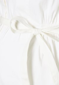 Vit klänning med figurnära liv och elastiskt midjeband, försett med ett matchande tygbälte som knyts framtill. Slät textur, minimalistisk design.