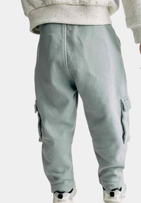 Lichtgrijze cargobroek van een katoenmix, met zijzakken en een elastische tailleband. Draagt bij witte en zwarte sneakers.