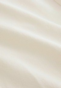 Texturerad krämfärgad tyg med ett slätt, ribbat mönster. Materialet verkar mjukt och lätt, och visar subtila variationer i färg och djup.