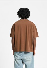 Brun oversized t-shirt med korte ærmer, lavet af blødt stof, med en rund halsudskæring og en lige kant, båret med lyseblå jeans.