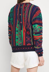 Neulottu villapaita, jossa on monivärinen kuvio punaisella, vihreällä ja sinisellä. Resorireunukset hihansuissa ja helmassa sekä teksturoituja yksityiskohtia kauttaaltaan.