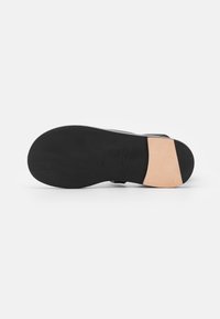 Soletta di scarpa nera con design piatto, caratterizzata da una texture di gomma liscia e un'accortezza in pelle beige vicino al tallone. Forma semplice e funzionale.