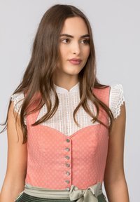 Rosa gemusterte Dirndl mit einer weißen Bluse mit Spitzenbesatz, die einen herzförmigen Ausschnitt und Knopfdetails aufweist, kombiniert mit einem grünen Rock.
