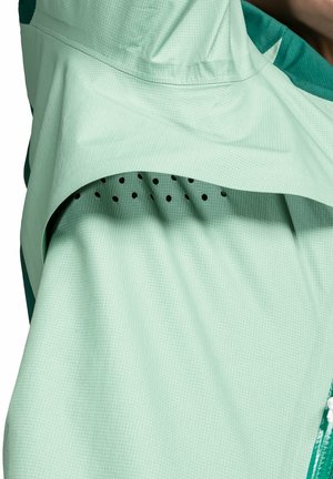 Lichtgroene jas van een gestructureerde stof, met een capuchon en ademend gaasventilatie detail. Inclusief zwarte perforaties voor ventilatie.