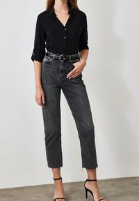 Camicia nera con bottoni e maniche arrotolate, abbinata a jeans neri a vita alta e taglio corto con orli sfrangiati. Accessori: cintura nera.