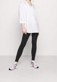 Vit oversized skjorta med knappar, svarta leggings och färgglada träningsskor med en blandning av vitt, rosa och teal accenter. Släta texturer överlag.