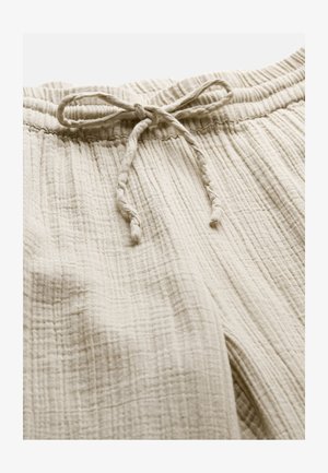 Hellbeige Textilhose mit Textur, elastischem Bund und vorne in der Mitte gebundenem Tunnelzug.