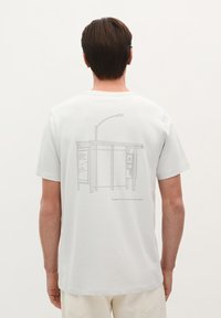 Lys grå T-shirt med et minimalistisk linjetegning af en busstoppested på ryggen med teksten "Scalpers Tours. Få din byguide."