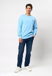 Svetlo modra mikica iz mešanice bombaža, s krojnim ovratnikom, z ribastimi manšetami, v kombinaciji s temno modrimi kavbojkami in belimi supergami. Črn logotip na prsih.