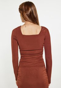 Top marrone a maniche lunghe a righe con scollatura quadrata e dettagli arricciati lungo la schiena, che creano una silhouette aderente.