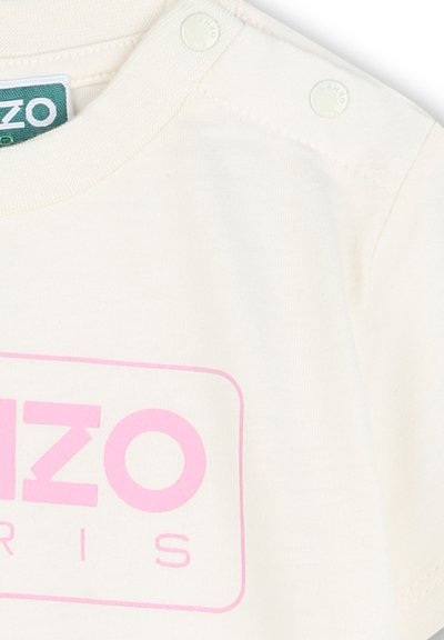 Korte mouwen, crèmekleurig katoenen t-shirt met een roze logo-print. Drukknopen op de schouder voor gemakkelijk aankleden. Gladde textuur.