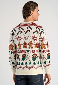 Witte gebreide trui met feestelijke patronen, waaronder peperkoekmannetjes, zuurstokken en kerstbomen in rode en groene tinten.