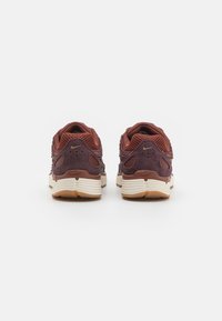 Pantofi sport maro și marsala din materiale mesh și piele suede, cu o talpă amortizată și o talpă exterioară din cauciuc bej; prezintă un mic logo auriu.