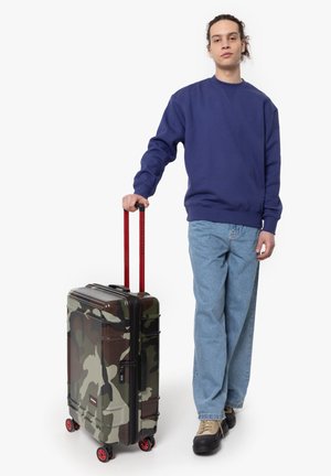 Camouflage hard-shell suitcase with red telescopic handle and wheels, featuring a textured surface and rectangular shape.