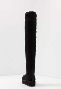 Czarne kozaki za kolano wykonane z miękkiej tkaniny o gładkiej fakturze, z płaską podeszwą na platformie i bocznym zamkiem błyskawicznym ułatwiającym zakładanie.