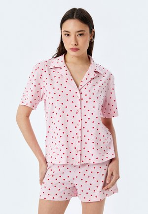 Schlafanzugset mit einem Kurzarm-Hemd mit Knöpfen und passenden Shorts. Hergestellt aus weichem rosa Baumwollstoff mit verstreuten roten Herzmustern.