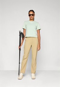 Šviesiai žalia trumpa palaidinė, smėlio spalvos kelnės ir balti sportbačiai. Laiko juodą vaikščiojimo lazdelę. Aksesuaras: tamsūs saulės akiniai. Paprastas dizainas.