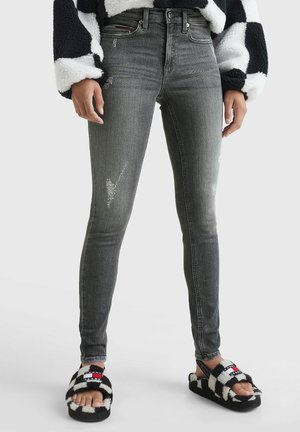 Vrouw draagt vervaagde grijze skinny jeans met versleten patch, zwart-witte harige geruite sandalen en zwart-witte harige mouwen van een jas.