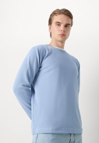 Camicia a maniche lunghe azzurro chiaro in tessuto testurizzato a costine con scollatura rotonda. Presenta un orlo dritto e cuciture laterali.