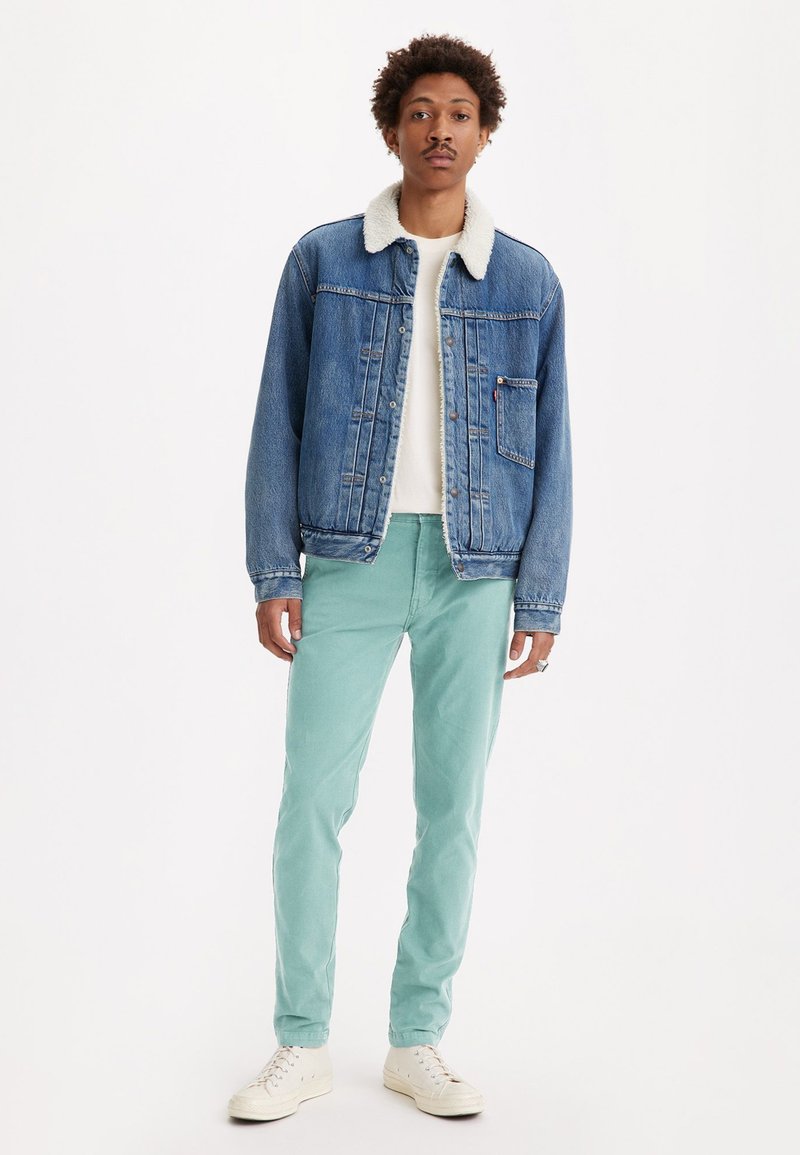 Chaqueta de mezclilla con cuello de borreguillo, color azul claro. Combinada con pantalones verde menta y zapatillas blancas. Diseño sencillo y corte relajado.